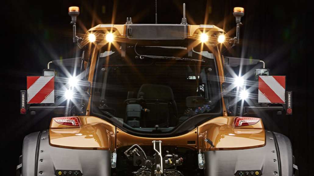 An orange Valtra S-Series tractor cab with its lights on.